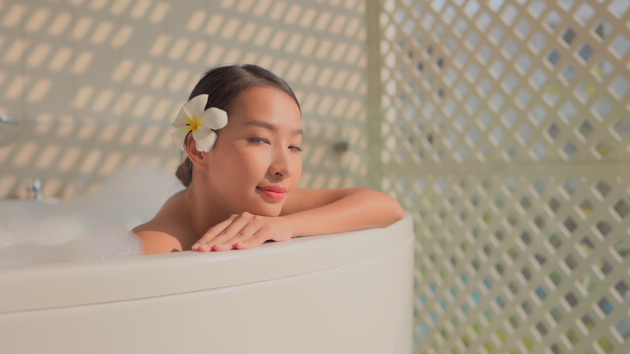 A beautiful Asian woman leans on her arm on the edge of a tub full of bubbles
