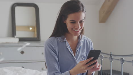 Woman-With-Mobile-Phone-Wearing-Pyjamas-Having-Video-Chat-Sitting-On-Bed