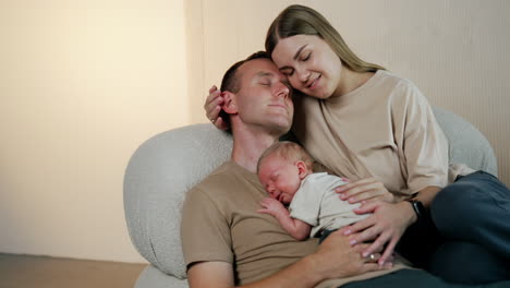happiness portrait. caucasian couple sitting on the sofa with a tiny newborn boy sleeping on dad's chest.