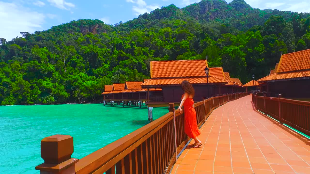 uma mulher relaxada numa casa de palafitas de um hotel de luxo olha para o mar na ilha de langkawi