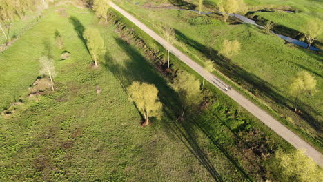 People-enjoy-sunny-day-while-riding-bicycle-in-nature-landscape,-aerial-follow-up-view