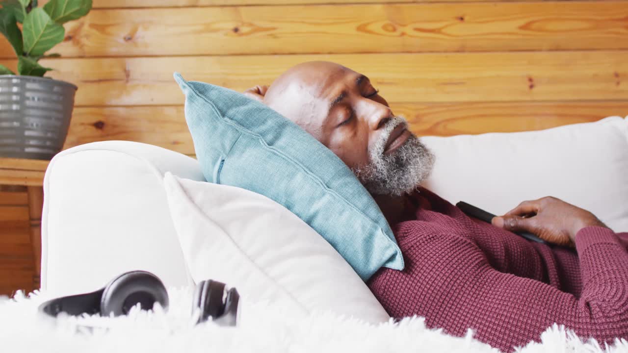 Uomo anziano afroamericano felice che trascorre del tempo in una baita in legno, mentre dorme sul divano, in slow motion.