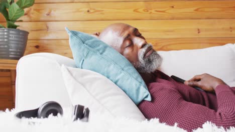 Happy-senior-african-american-man-spending-time-in-log-cabin,-sleeping-on-sofa,-slow-motion