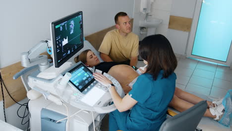 caucasian couple is in the obstetrician cabinet. doctor checking the pregnant woman on ultrasound equipment. top view.