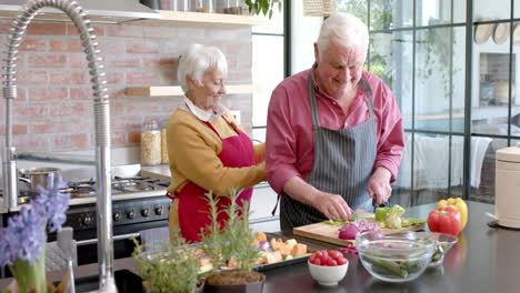 Feliz-Pareja-Caucásica-Mayor-Usando-Delantales-Cocinando-La-Cena-En-La-Cocina-De-Casa,-Cámara-Lenta