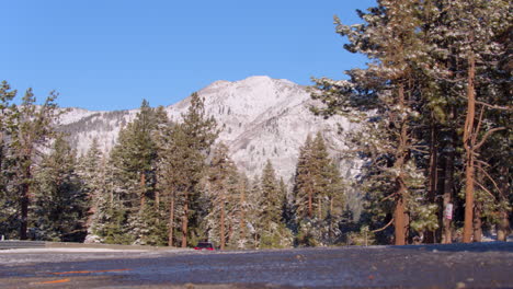 Low-angle-view-of-a-mountain-and-trees-in-Lake-Tahoe-from-side-of-the-road-with-cars-driving-past