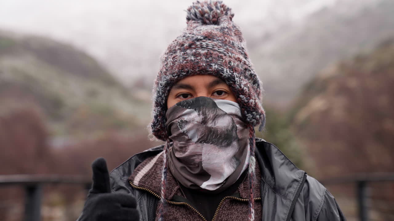 A man adjusts his warm winter beanie, with his face covered by a mask and wearing gloves, on a snowy day in Patagonia, Chile.