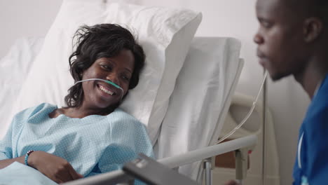 the patient smiles at the good news from the doctor lying under the iv and breathing apparatus. a young african-american male doctor is talking to a patient. a black woman patient talks to a doctor