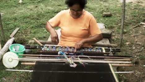 a middle-aged woman in a yellow shirt is weaving traditional cloth in wae rebo village, one of the tallest villages in indonesia.