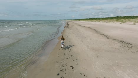 Aerial-view-with-a-young-longhaired-girl-riding-a-bike-on-the-sandy-beach,-sunny-day,-white-sand-beach,-active-lifestyle-concept,-wide-drone-shot-moving-forward