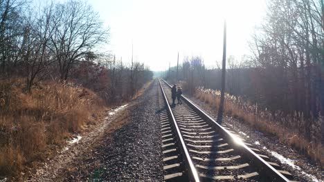 Backside view of two boys walking on a rail. Children are going along the railroad in a sunny winter day. Danger concept.