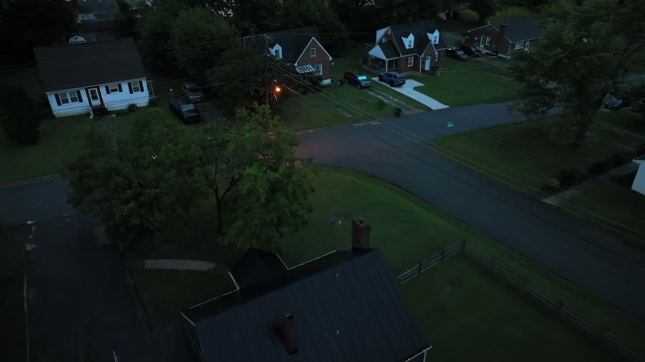 Aerial flyover American neighborhood at dark clouds and rainy day. Suburb residential area with houses and lighting lanterns. Bin on street. Landing shot