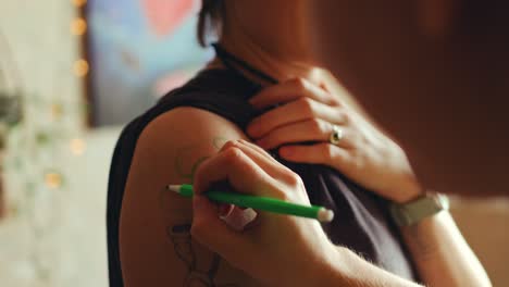 female tattoo artist drawing design on arm of woman