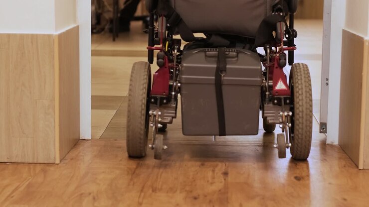 A man in a wheelchair drives down the hallway. A person with a disability moves around the hospital.
