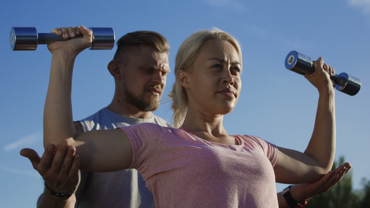Woman and trainer performing shoulder press outdoors