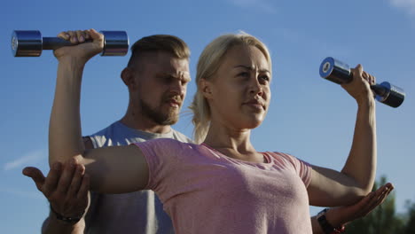 woman and trainer performing shoulder press outdoors