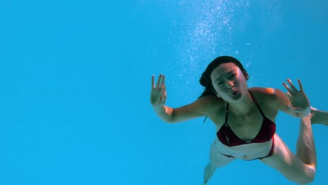 bruneta feliz saludando a la cámara bajo el agua en la piscina