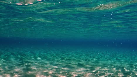 Escena-Real-Bajo-El-Agua-De-Aguas-Cristalinas-Del-Océano-Tropical-Turquesa-Con-Superficie-Ondulada-Y-Reflejos-En-El-Fondo-Marino-Con-Fondo-Azul