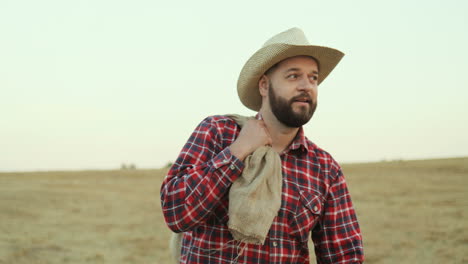 young farmer putting a sack with grain on his shoulder and carrying it in the field