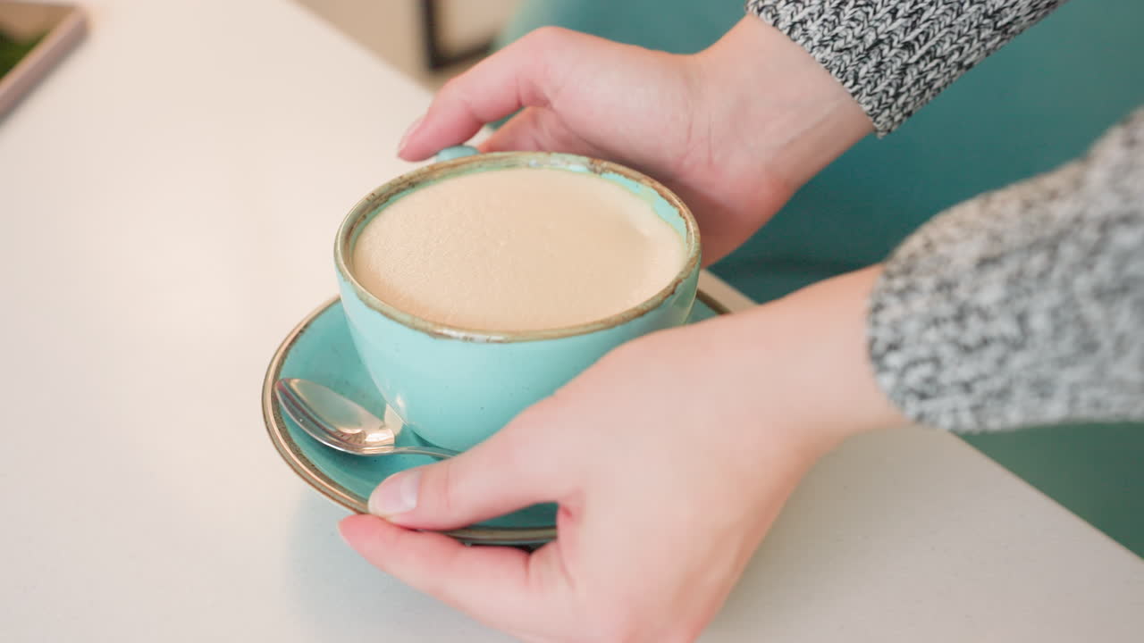 a young woman walking toward table with hot tea held in both hands carefully sitting down adjusting cup and saucer gently cozy indoor setting soft lighting calm relaxing atmosphere warm vibe