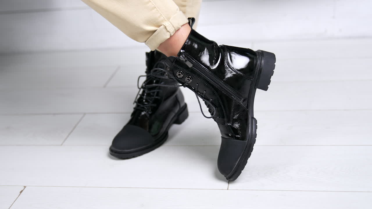 Female wearing black lacquered boots with opaque nosepieces. Model stands and turns around in her comfortable stylish footwear. Close up.