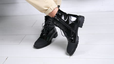 female wearing black lacquered boots with opaque nosepieces. model stands and turns around in her comfortable stylish footwear. close up.