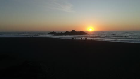 sunset in ocean with silhouetted people walking on the beach aerial