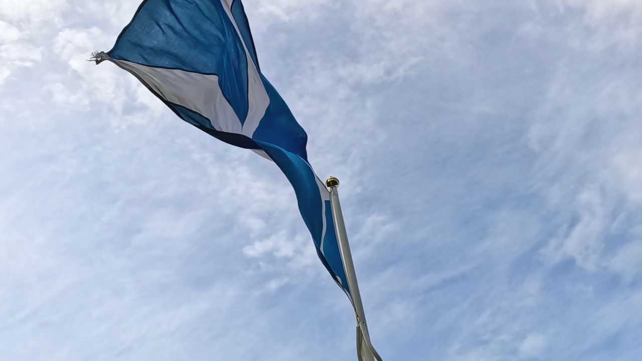 A blue and white flag gracefully waves against a backdrop of a partly cloudy sky.
