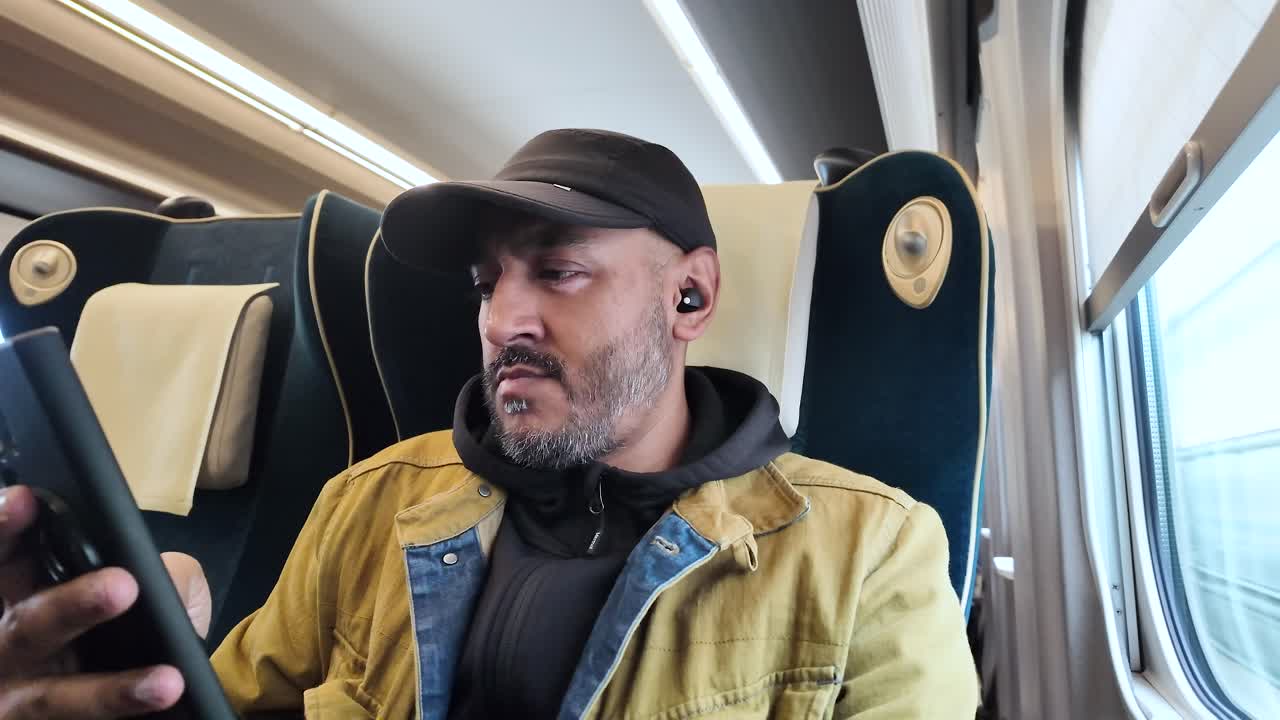 Bearded south asian man wearing earbuds using mobile phone while traveling on train