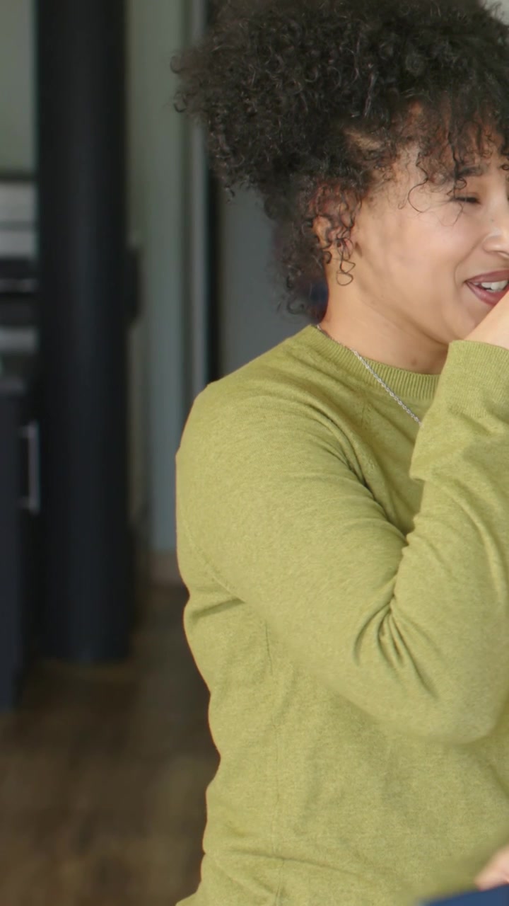 Vertical video: Turning woman smiling and laughing, covering mouth, reacting to blue phone at home