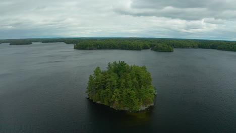 drone shot of small island in the middle of a lake with a cottage on it on a dreary, cool day