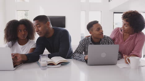 Middle-aged-black-parents-helping-their-teenage-kids,-using-laptops-to-do-their-homework,-front-view
