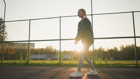 young lady in hoodie playing volleyball in outdoor setting with sunlight radiating from the distance, open field in the background, and someone playing in the distance
