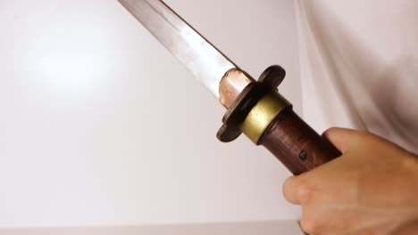 pulling antique sword from sheath in white room close up