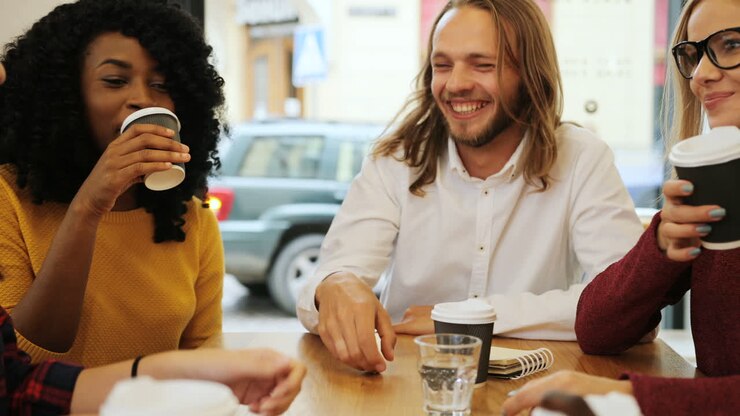 gruppe multiethnische gruppe glücklicher freunde, die lachen und ein video auf einem telefon ansehen, das an einem tisch in einem café sitzt
