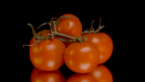 Langsam-Rotierende-Tomaten-Zeigen-Einzelne-Früchte-In-Einer-Glatten-Filmischen-Nahaufnahme,-Gefilmt-In-Slomo-Vor-Einem-Schwarzen-Hintergrund-Auf-Einer-Verspiegelten-Oberfläche