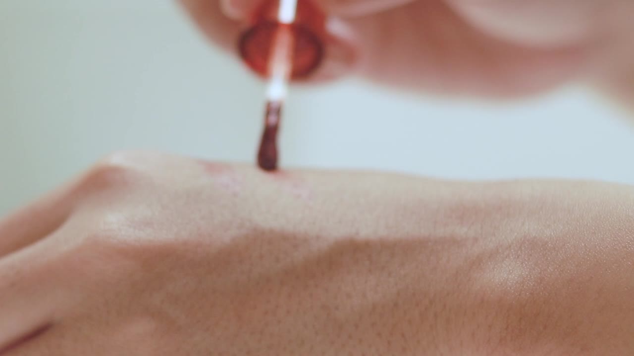 Close up of testing a tube of red lip tint and swatching it on the back of a hand to check the color