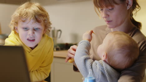 busy mom using laptop while sitting with kids at home