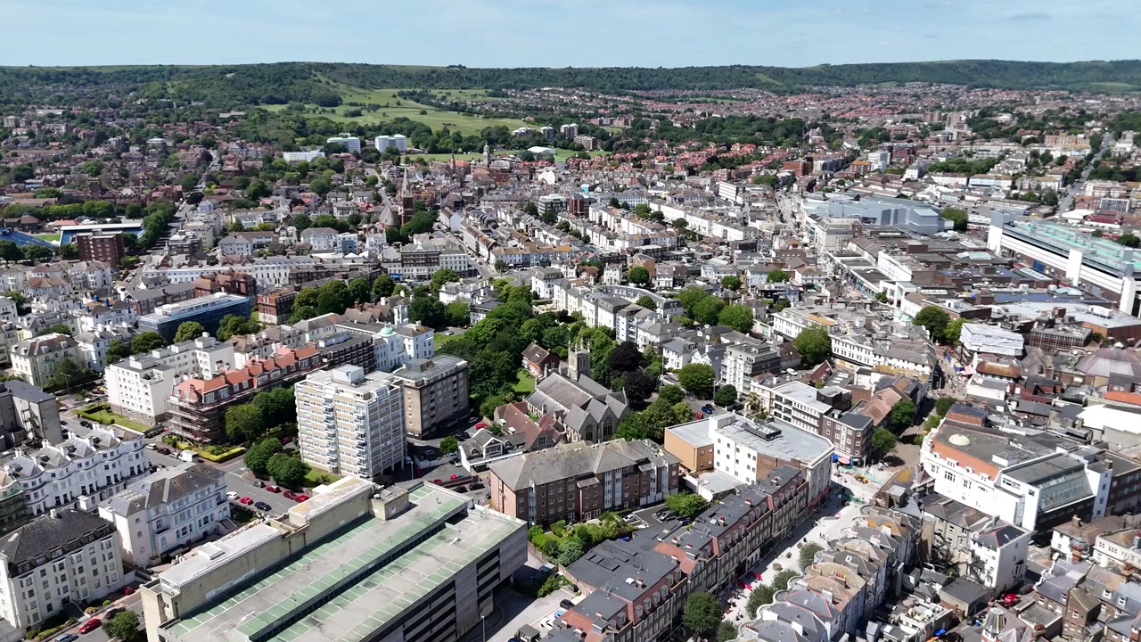 Filmischer Drohnen-Überflug vom Eastbourne Pier und Strand ins Stadtzentrum von Eastbourne, der belebte Einkaufsstraßen, die Strandpromenade und lebhaften Küstentourismus in 4K zeigt.
