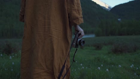 Back-shot-following-a-Person-walking-in-nature-wearing-a-orange-robe-holding-a-camera