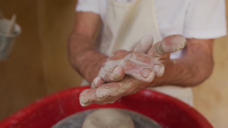 hombre caucásico mayor que usa un delantal y limpia las manos en un taller de cerámica