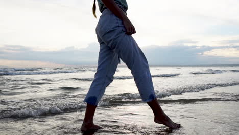 Pretty-young-female-walking-on-sandy-coastline-and-ocean-waves,-close-up-view