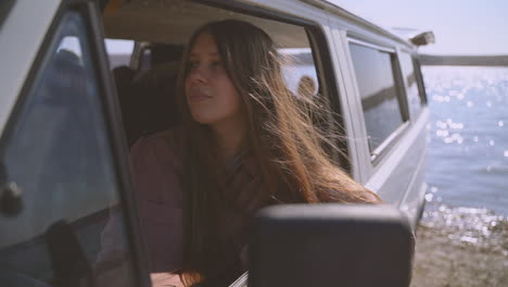 a young long haired red haired girl sitting in a caravan by a lake looks around