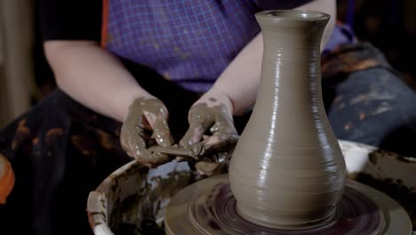 close up shot of the woman's hands, the mater forms the shape of a clay pot with tools, the product stands on a potter's wheel