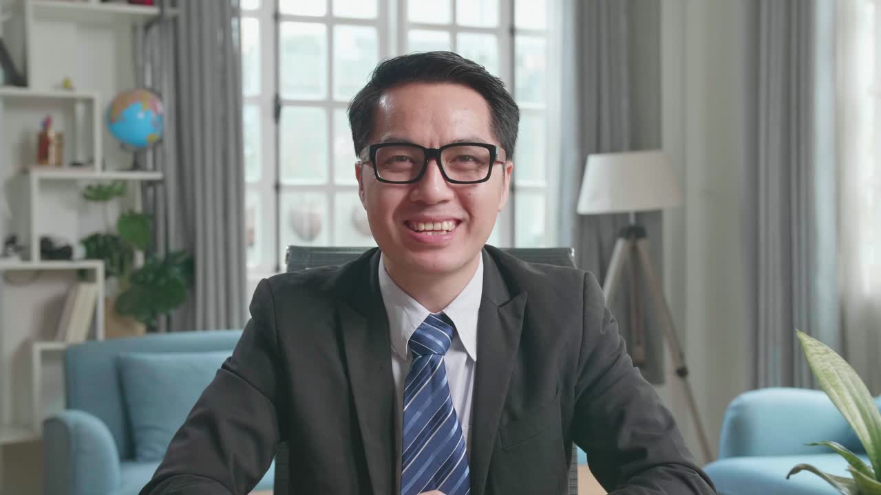 Asian Businessman With Glasses Wearing Business Suit Talking On The Video Call While Working At Home.