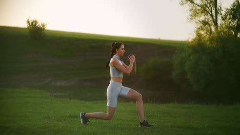 una mujer camina por la hierba en un parque realizando estocadas alternas en cada pierna en movimiento al atardecer en verano