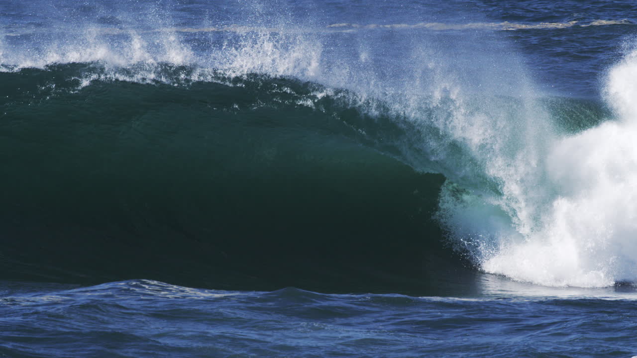Dark barreling wave rolls in with backlit spray and textures of ocean power