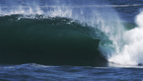 dark barreling wave rolls in with backlit spray and textures of ocean power
