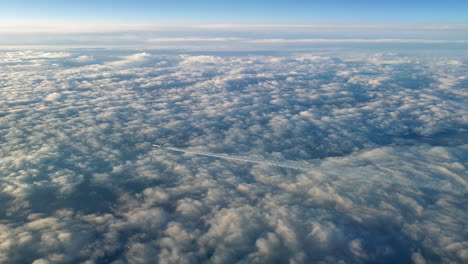 Vista-Increíble-Desde-La-Cabina-De-Un-Avión-Que-Vuela-Alto-Por-Encima-De-Las-Nubes-Dejando-Un-Largo-Rastro-De-Aire-De-Vapor-De-Condensación-Blanco-En-El-Cielo-Azul