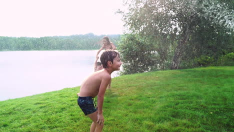 Mom-dad-and-two-sons-in-the-summer-on-the-grass-poured-water-from-a-hose-for-the-lawn.-Area-country-house-near-a-lake-at-sunset